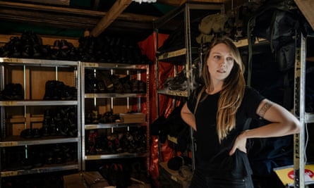 A woman stands in a dark storage room with shoes on shelves behind her
