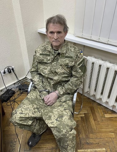 Image of a man looking worn out, wearing green military fatigues and sitting in a metal chair in a white room.