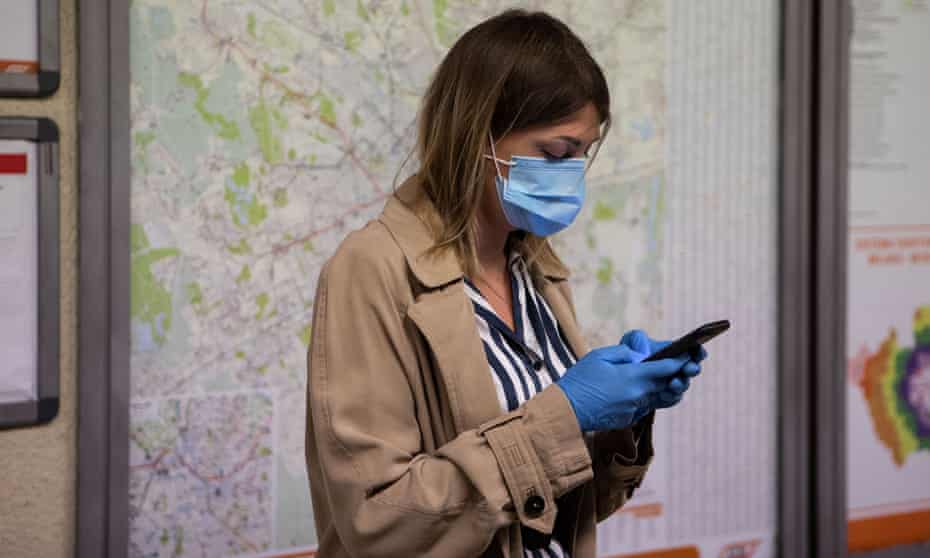 A woman wearing a mask and gloves uses a mobile phone while waiting for an underground train in Milan, Italy