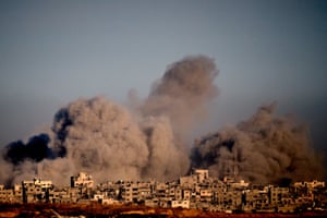 Huge clouds of grey smoke rise behind residential buildings, some of which are damaged