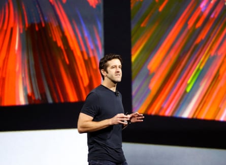 John Ternus speaks in front of screens displaying graphics in a bright orange ray-like pattern.