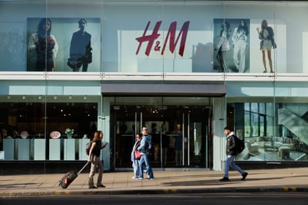 Frontage of an H&M store in Edinburgh. People are walking in front of the doors, including a woman pulling a wheelie case.