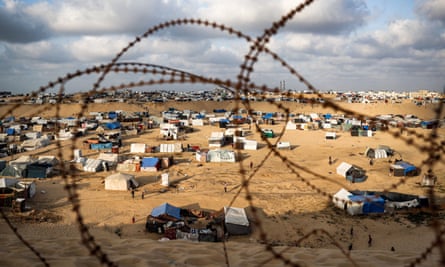 View through barbed wire to makeshift shelters, including pitched tents, near a city in Israel