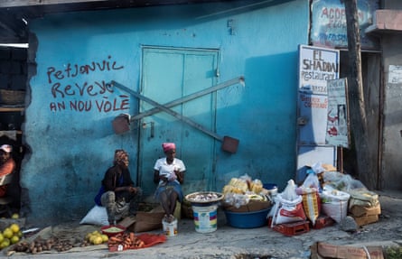 Street traders sit in front of political graffiti in Pétion-Ville on the outskirts of Port-au-Prince