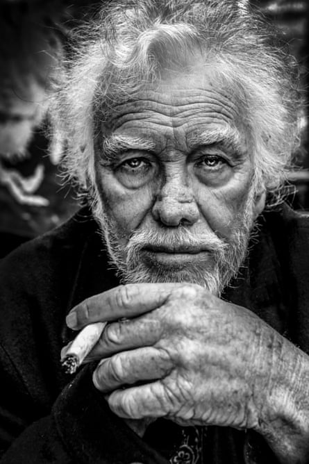 A man stares into the lens, holding a cigarette in a black and white photo