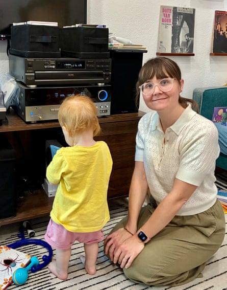 Gabriela Crowley wearing glasses smiles beside a toddler facing a stack of stereo equipment