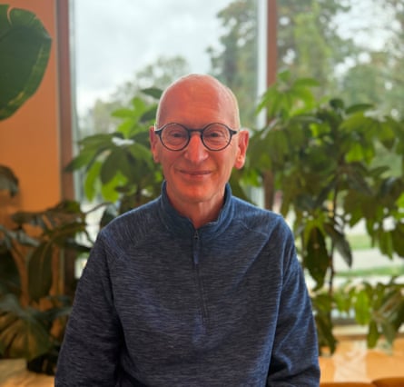 Giles Gibson sitting in front of a window at his home with plants in the background