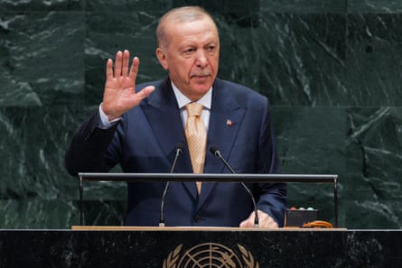 A man in a suit and tie addresses an audience from behind a podium mounted with microphones.