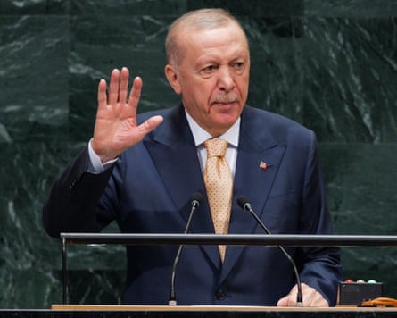 A man in a suit and tie addresses an audience from behind a podium mounted with microphones.