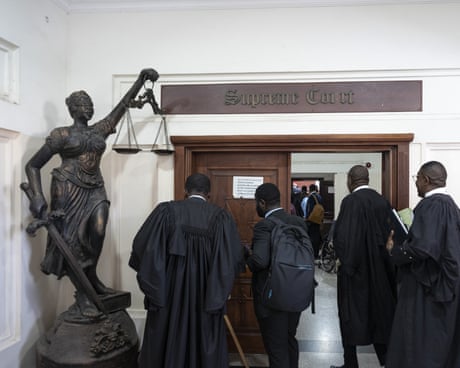 Lawyers in black gowns seen by a statue of lady justice holding scales and a sword