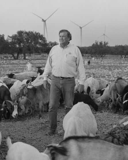black and white photo of a man surrounded by goats standing for a portrait in front of wind turbines