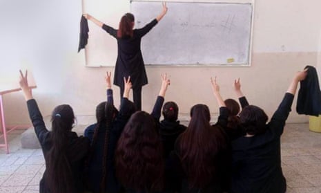 Schoolgirls with their backs to the camera remove their hijabs in a classroom in a protest in Iran.