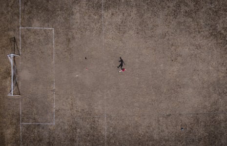 An aerial view showing a person’s shadow on a parched football field.