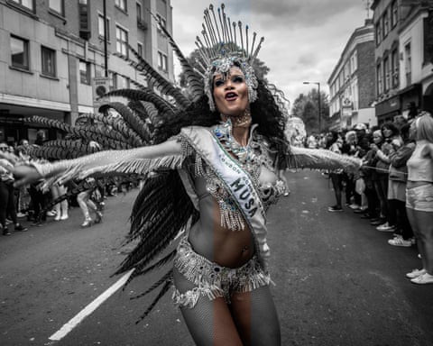 Patsy in an elaborate feathered costume and jeweled headdress dances at a street carnival