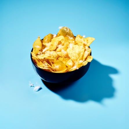 Crisps in a black bowl with cotton remnants sprinkled over the top and a couple next to the bowl, against a sky-blue background