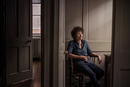 A woman with a curly hair wearing a blue shirt sitting in a room with taupe walls