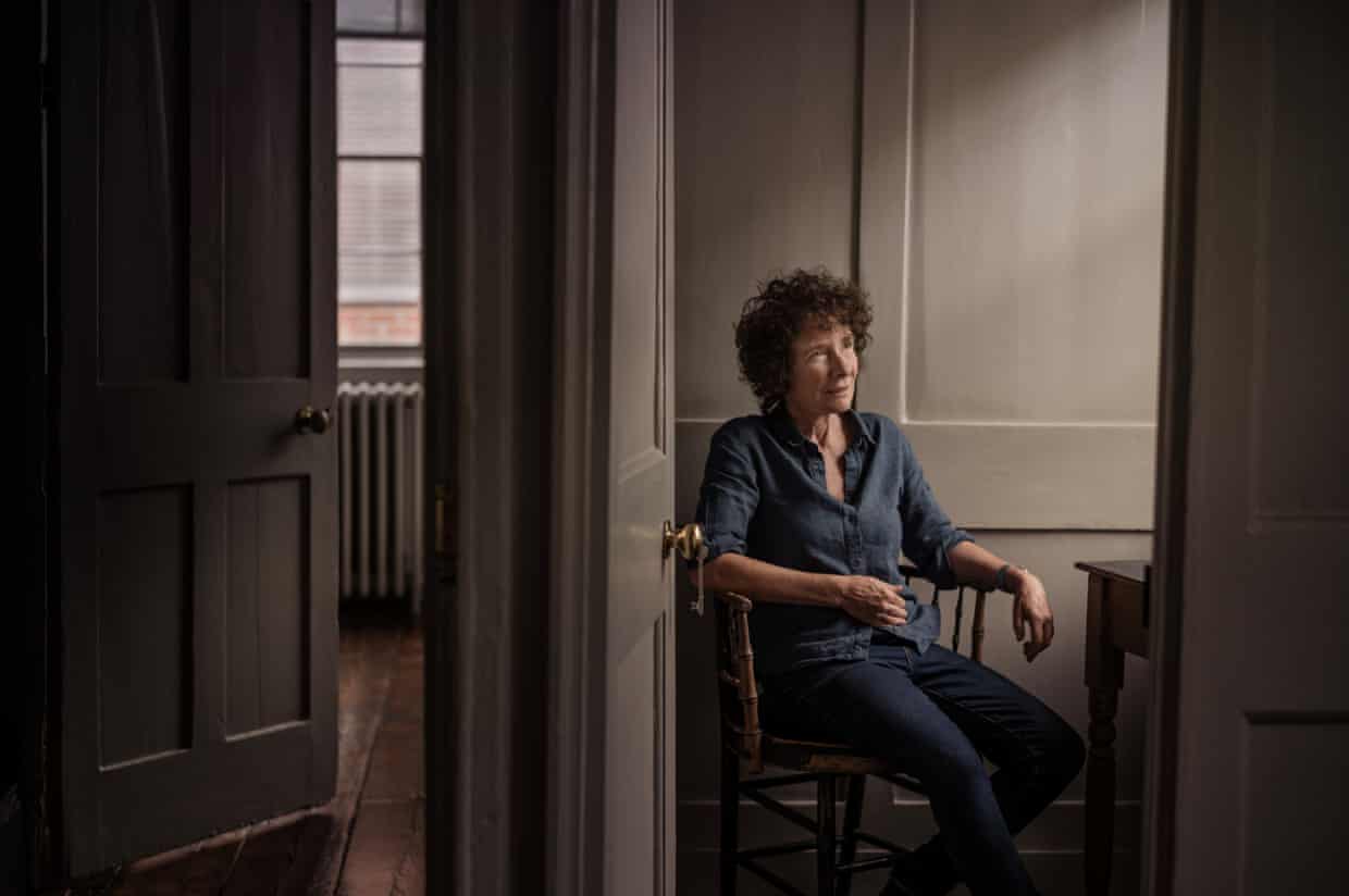 A woman with a curly hair wearing a blue shirt sitting in a room with taupe walls