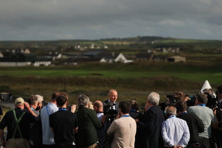 Micheál Martin surrounded by members of the press on a golf course.