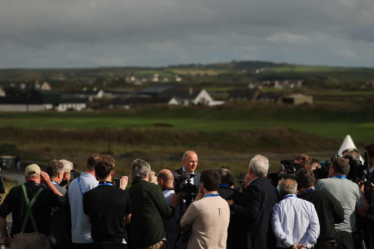 Micheál Martin surrounded by members of the press on a golf course.