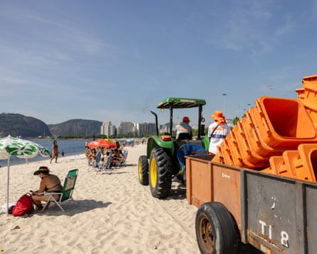 A tractor pulls a cart of orange bins along a sandy beach