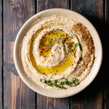 Hummus with olive oil and ground cumin in ceramic bowl over dark wooden background. Top view, flat lay