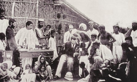 A man is surrounded by people who live in an Indian village and he is injecting a child with a vaccine.