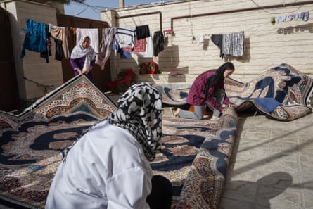 Women unroll a carpet in a courtyard.