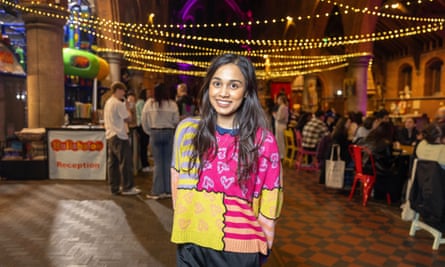 Taz stands in the middle of the church; she has long dark hair and wears a brightly coloured and patterned jumper. Other attenders are in the background