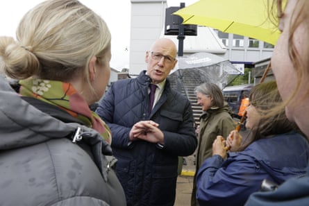 Hamilton, centre, speaks to a couple of potential voters outside as one holds a yellow umbrella