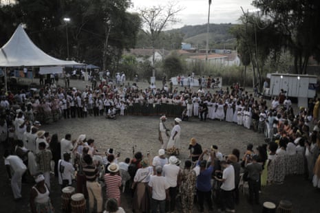 An overhead, twilight view of dozens of people in a wide circle, most of African descent and wearing white, with a man and a woman in the center.