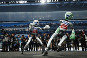 People look on as a robot with a padded helmet and gloves delivers a blow to another robot