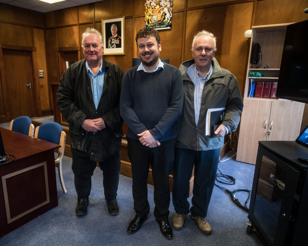 Three Falkland Islands assembly members stand smiling together in a wood-panelled office