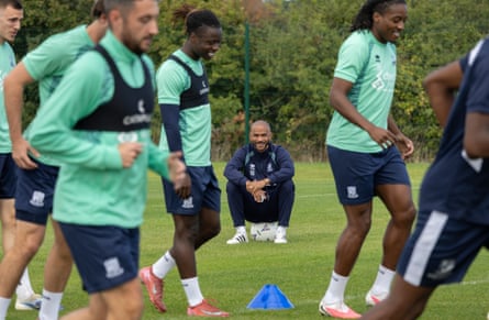 The Southend manager, Kieron Dyer, sits on a ball smiling as his players run past.