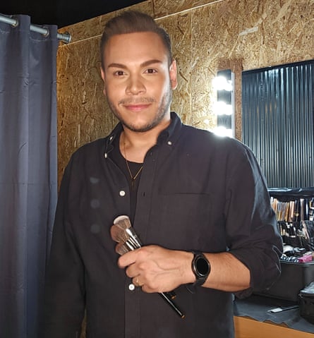 A Venezuelan man dressed in a black shirt holding makeup brushes.