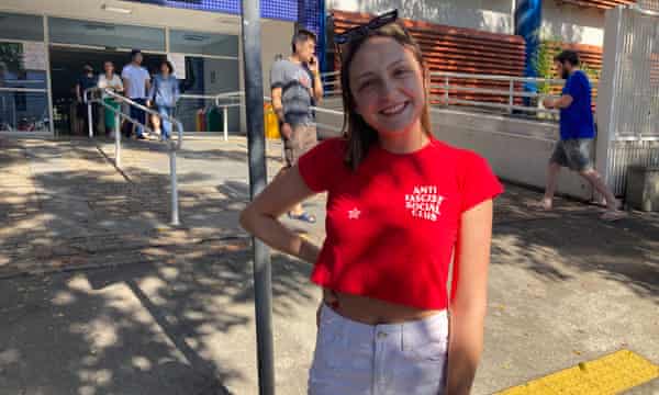 Gabriele Tissot Zappalá, wearing a red T-shirt with the words 'Anti-fascist Social Club', smiles as she stands outside a Paulista University building
