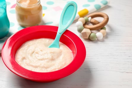 Baby food in a red plastic bowl with a turquoise spoon in it.