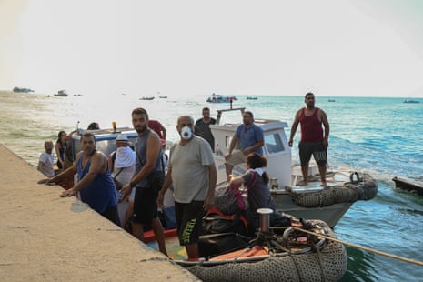 People board two boats moored to a dock while smoke hangs in the air.