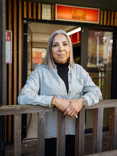Diana Sach, in a light shirt, leans on wooden railing outside a timber-clad retail unit