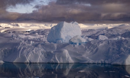 An eroded type of iceberg in Antarctica sits on water against the backdrop of a stormy gray sky
