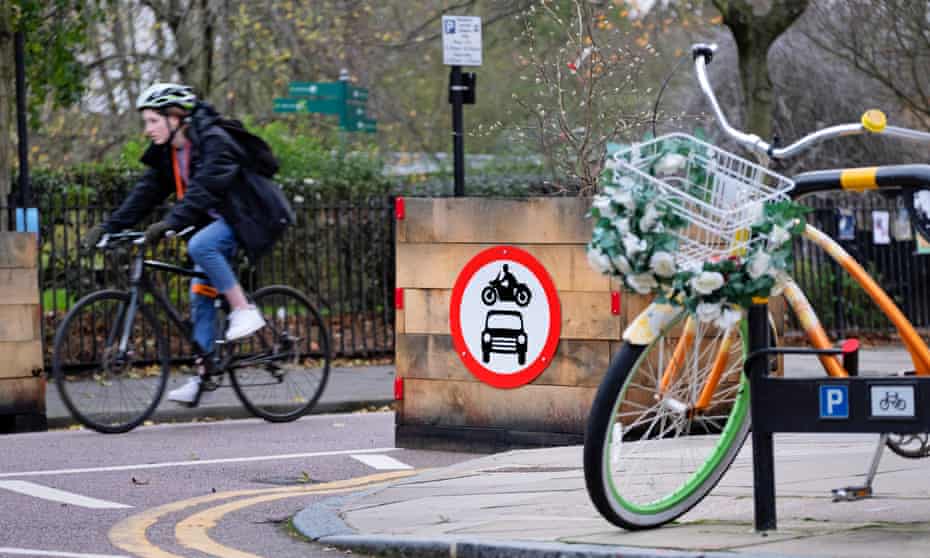A cyclist passes a wooden planter restricting access to cars and motorbikes into a low-traffic neighbourhood in London