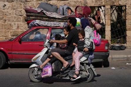 A man, woman and three children ride a motorbike past a car with personal belongings piled on its roof