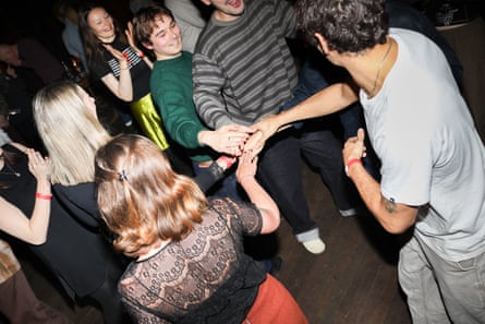 Young men and women dancing. They are holding their hands together in the centre of a circle. They are dressed informally with the men in jeans and T-shirts.