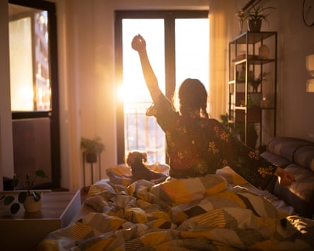 Young woman stretching in bed in the morning while looking at the sunrise