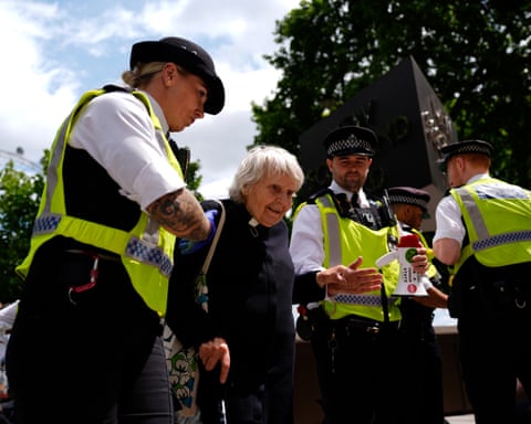 A police officer escorts Reverend Sue Parfitt past other officers at a demonstration