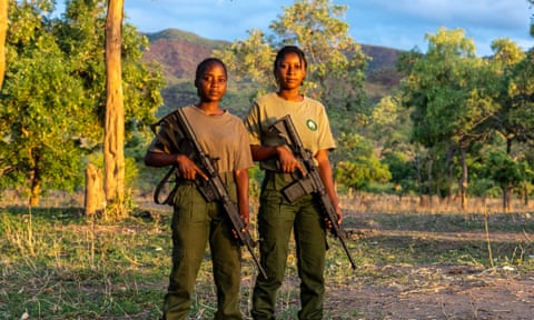 The two women holding sophisticated looking rifles against the backdrop of the beautiful national park