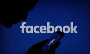 Person looking at Facebook logo on mobile phone
