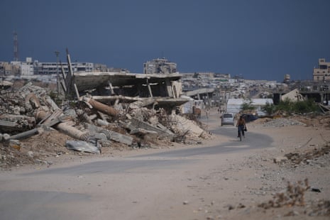 A Palestinian man rides his bicycle by the rubble of buildings that were destroyed in Israeli strikes.