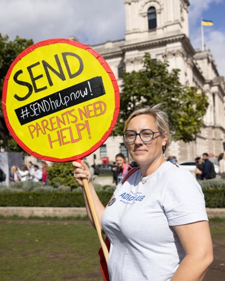 she holds up a yellow circular sign with red edging that looks like a lollipop road crossing patrol's; written on it is Send help now, parents need help'. She has blond hair and glasses and wears a white T-shirt with lettering that reads 'ADHD club'.