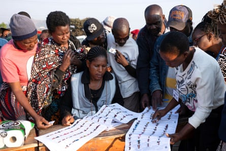 A group of people stand around a table looking at names on a paper list.