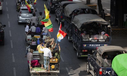 Supporters of the Myanma military drive by police trucks parked in Yangon.